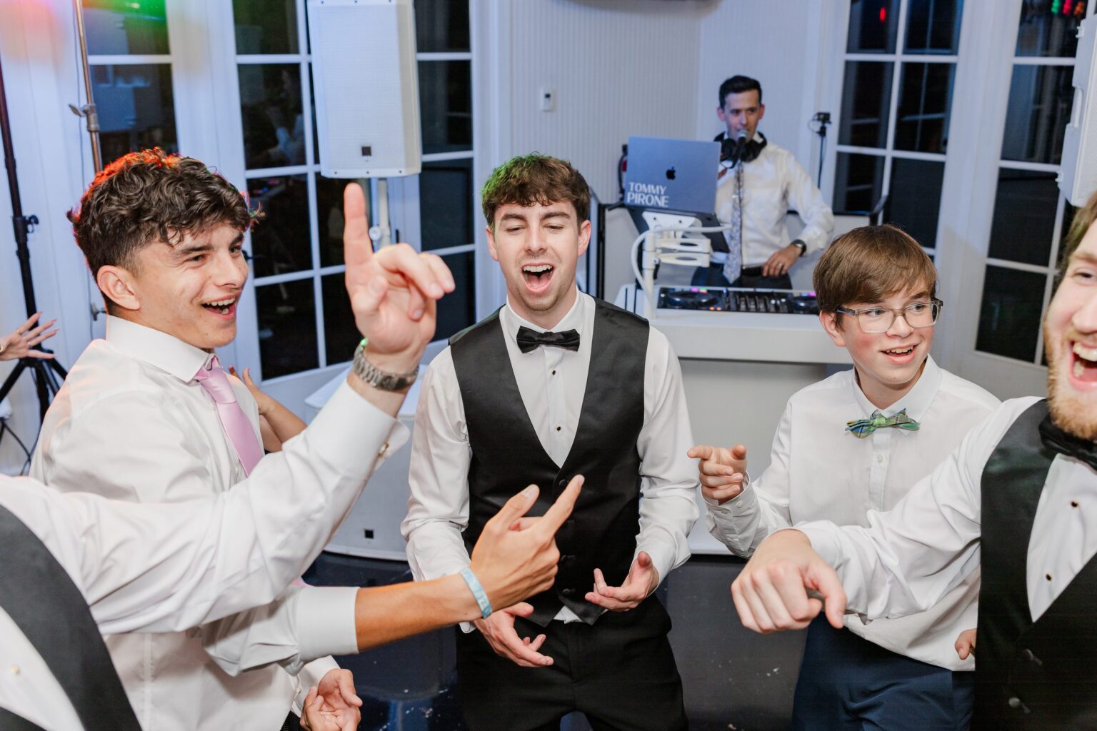 Groom and groomsmen singing in a circle while DJ Tommy Pirone plays at the DJ booth at a Little River Farms wedding in Alpharetta GA