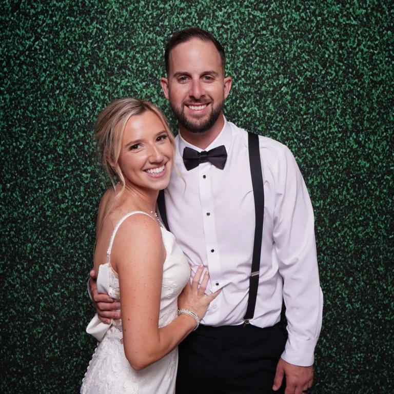 Bride and groom posing in front of a green grass wall photo booth backdrop — Pirone Entertainment