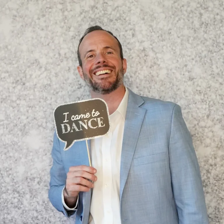 Smiling wedding guest in a light blue suit holding an "I came to dance" prop sign in front of a silver sparkle photo booth backdrop — Pirone Entertainment