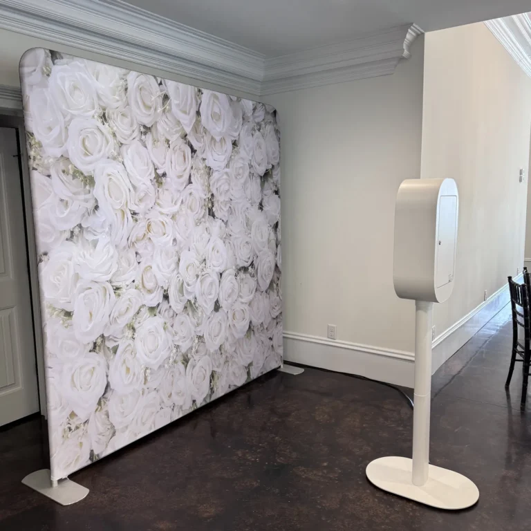 White photo booth next to a white roses flower wall backdrop at a wedding venue — Pirone Entertainment