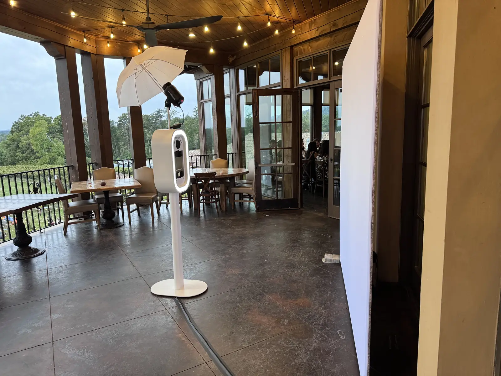 White photo booth with lit ring screen and flash umbrella on the covered terrace at Montaluce Winery & Vineyards, with string lights and vineyard views — Pirone Entertainment