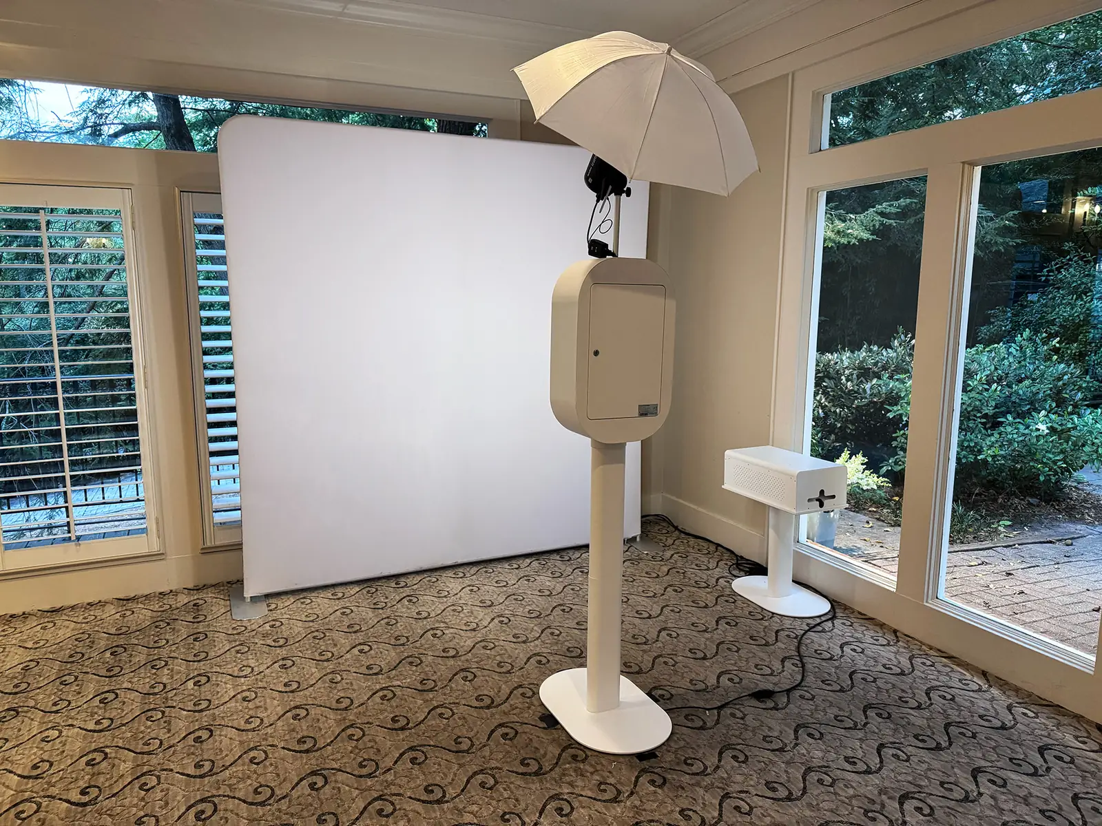 White photo booth with flash umbrella, print station and white fabric backdrop set up in a sunroom at Primrose Cottage — Pirone Entertainment